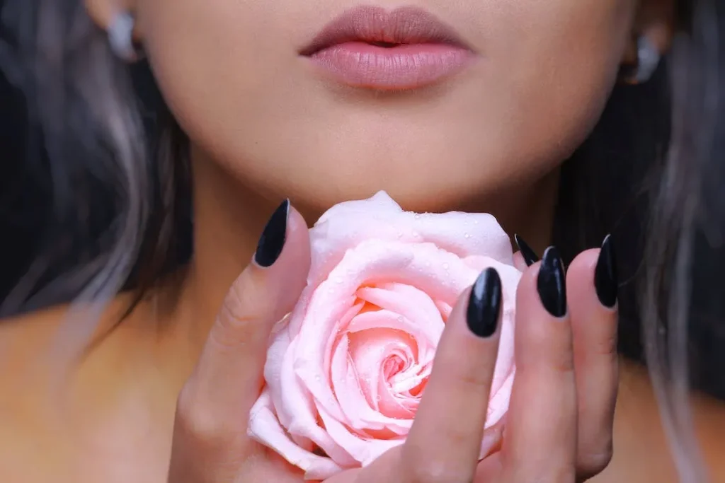 女性の唇と手にもったピンクのバラ